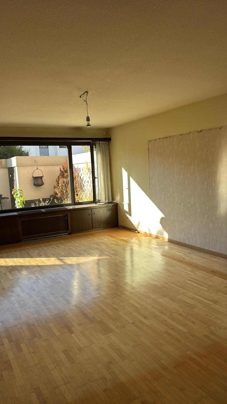 Leeres Wohnzimmer mit Parkett nach der Haushaltsauflösung, Blick zum Gartenfenster
