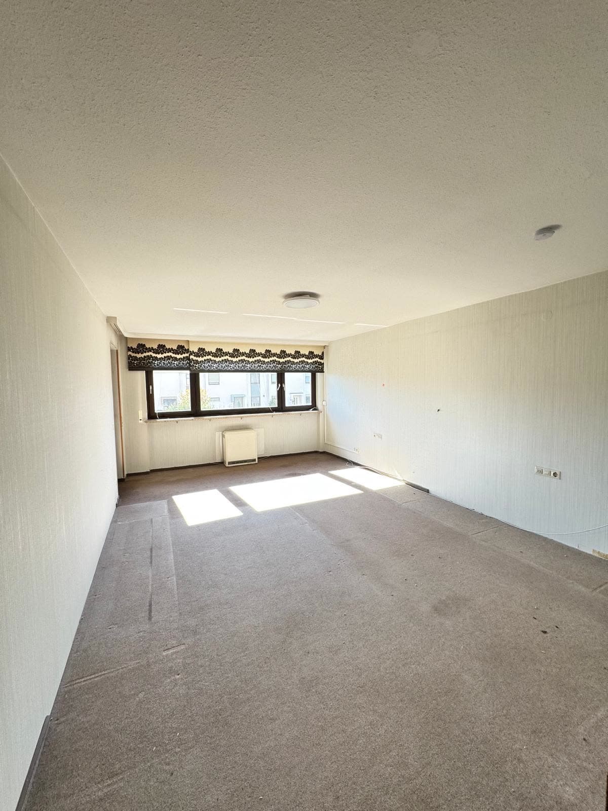Leeres Wohnzimmer mit Teppichboden und Fensterfront nach der Wohnungsauflösung